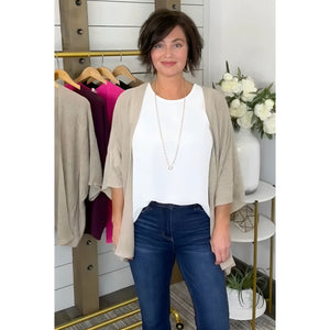 A woman wearing a pink kimono cardigan over a white top, paired with blue jeans. She is accessorized with a necklace and earrings.
