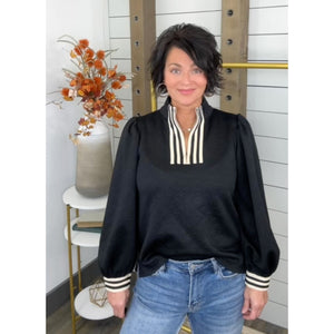Woman wearing a black top with striped cuffs and trim, standing indoors.